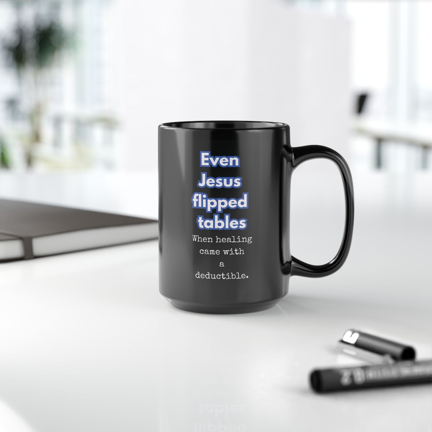Black mug with humorous text on a desk with office items.