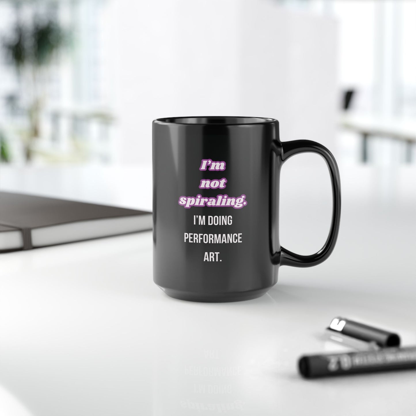 Black mug with humorous text on a desk with office items.