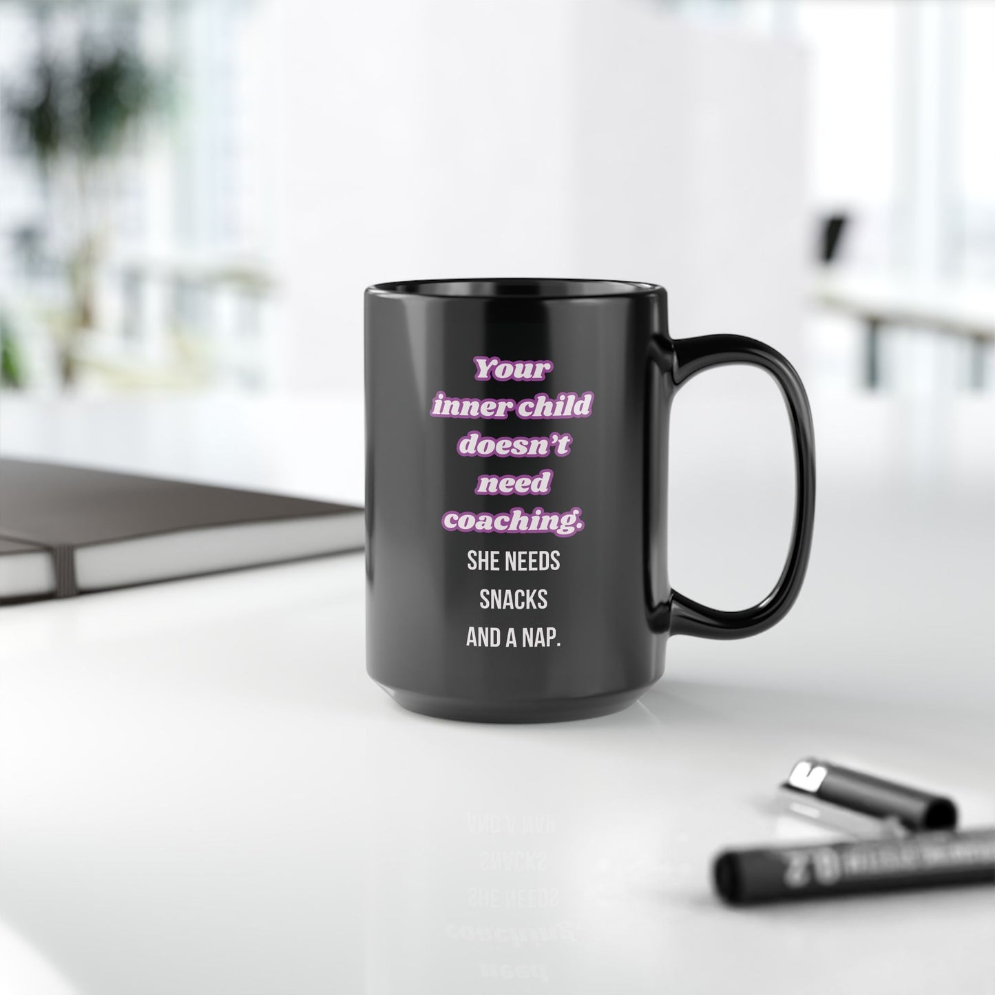 Black mug with humorous text on a white surface with office items.