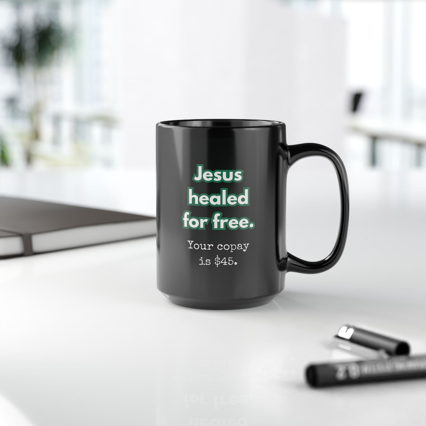 Black mug with text on a white surface with office items