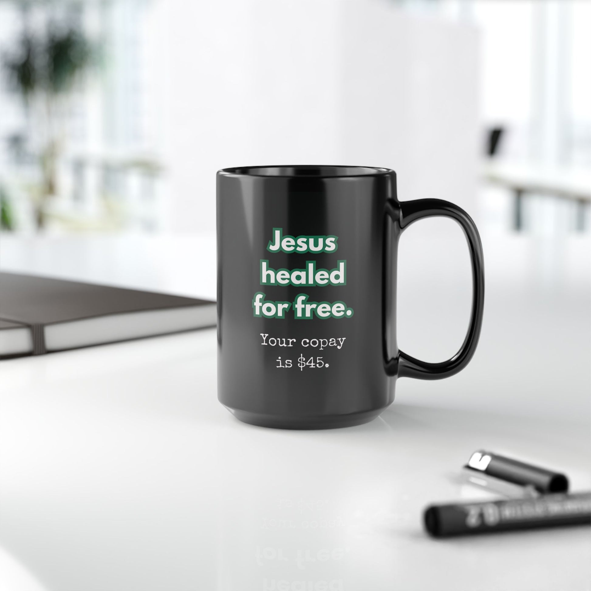 Black mug with text on a white surface with office items