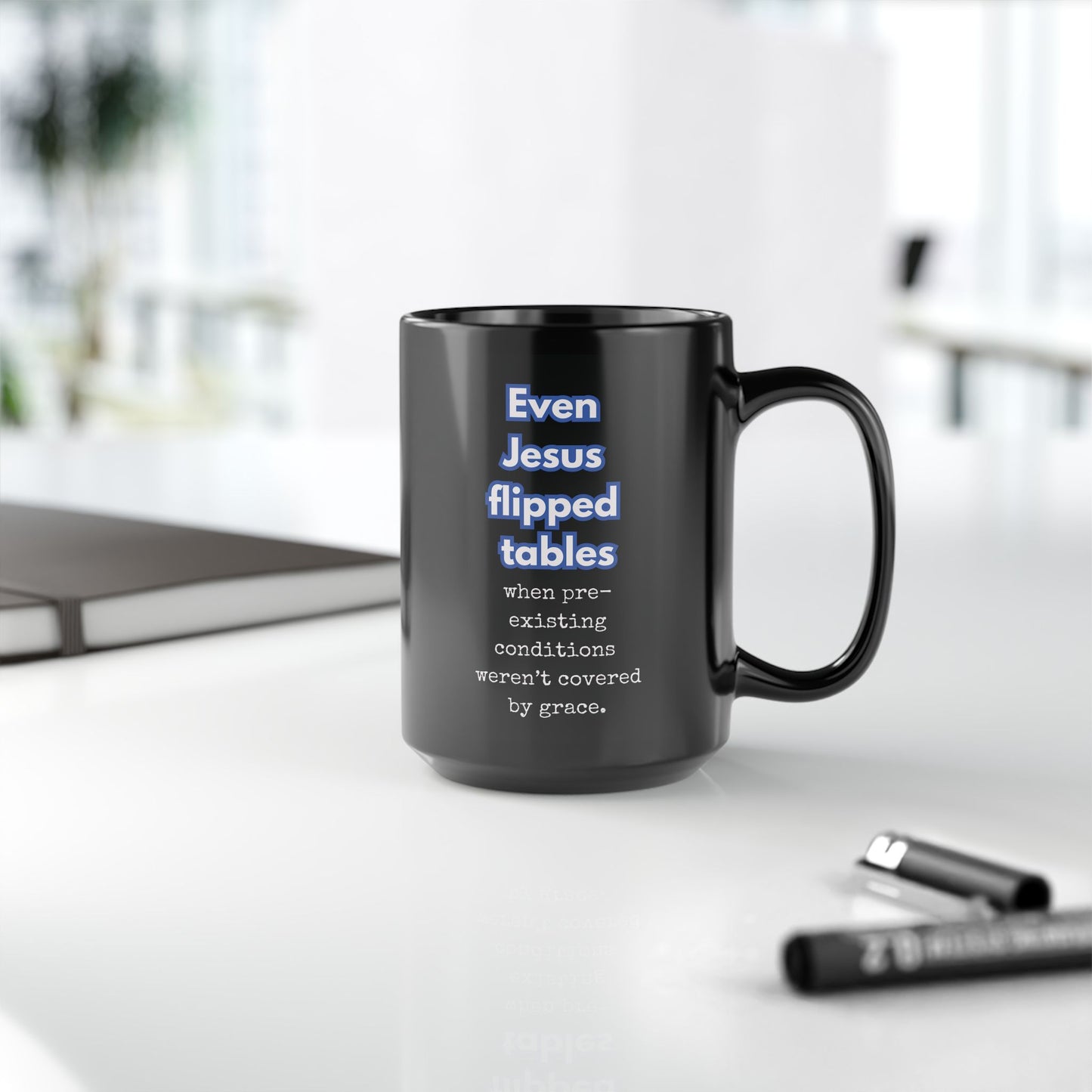 Black mug with humorous text on a white surface with office items.