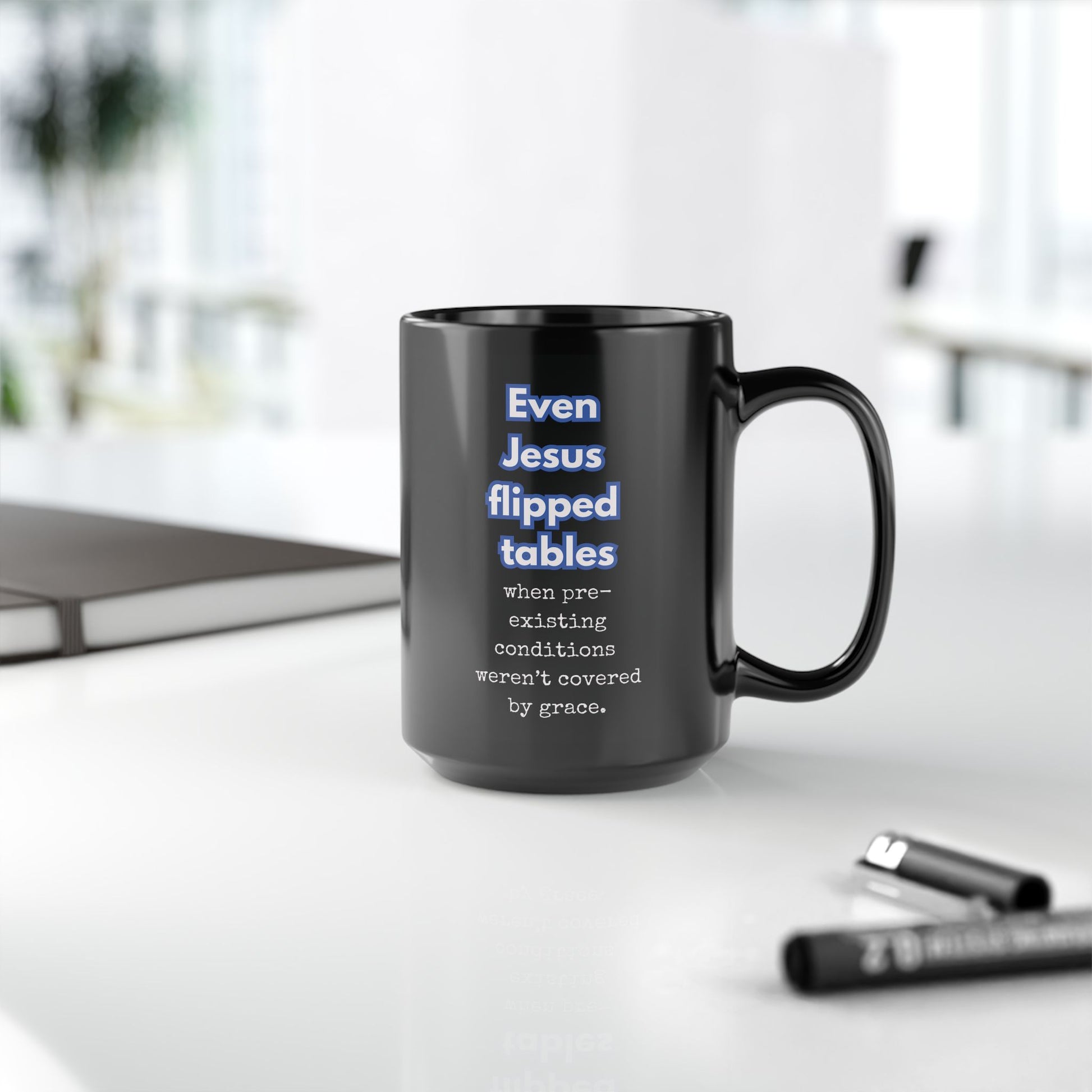 Black mug with humorous text on a white surface with office items.
