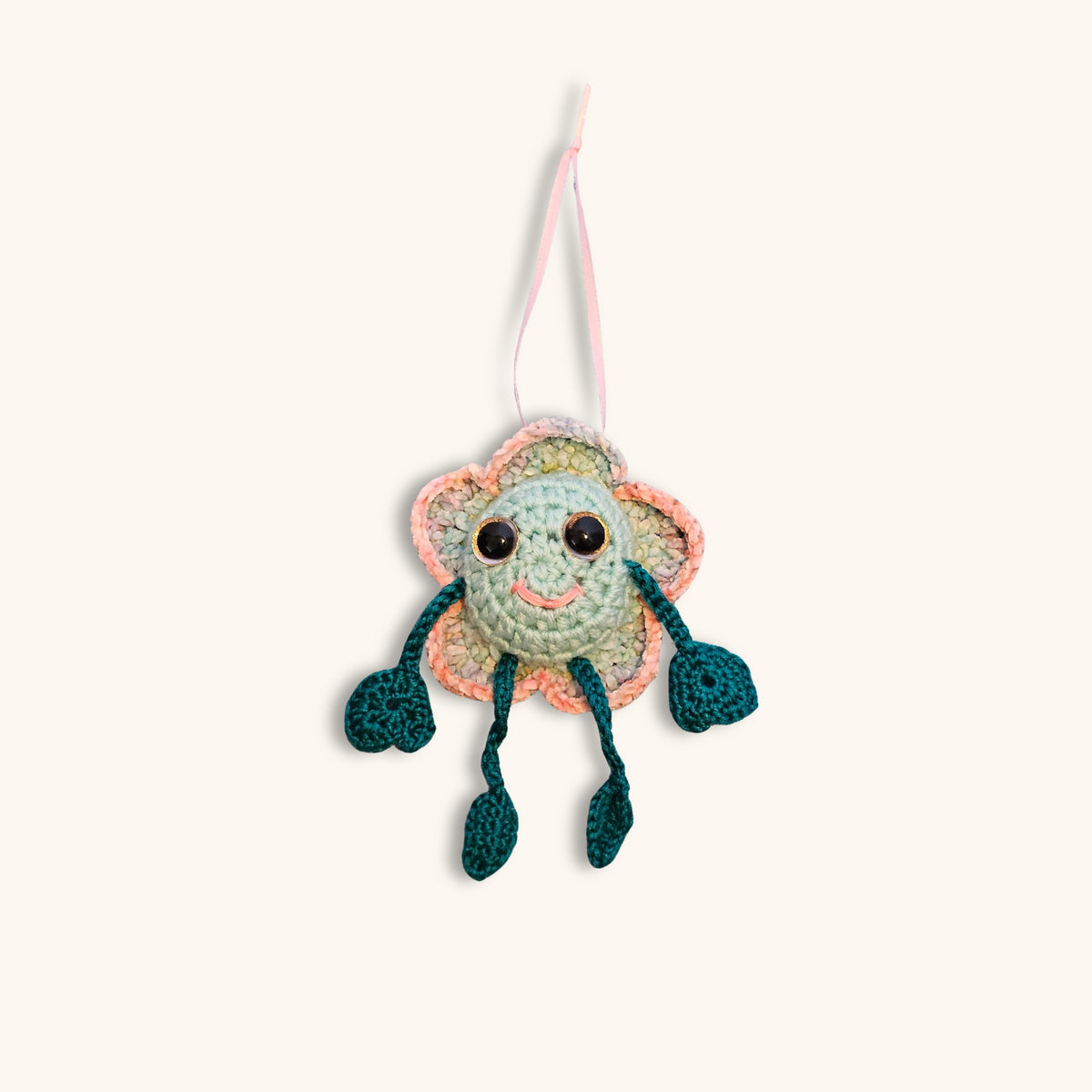Full front view of Floyd Flower Boy hanging from a pink ribbon as a whimsical handmade crochet decorative keepsake.