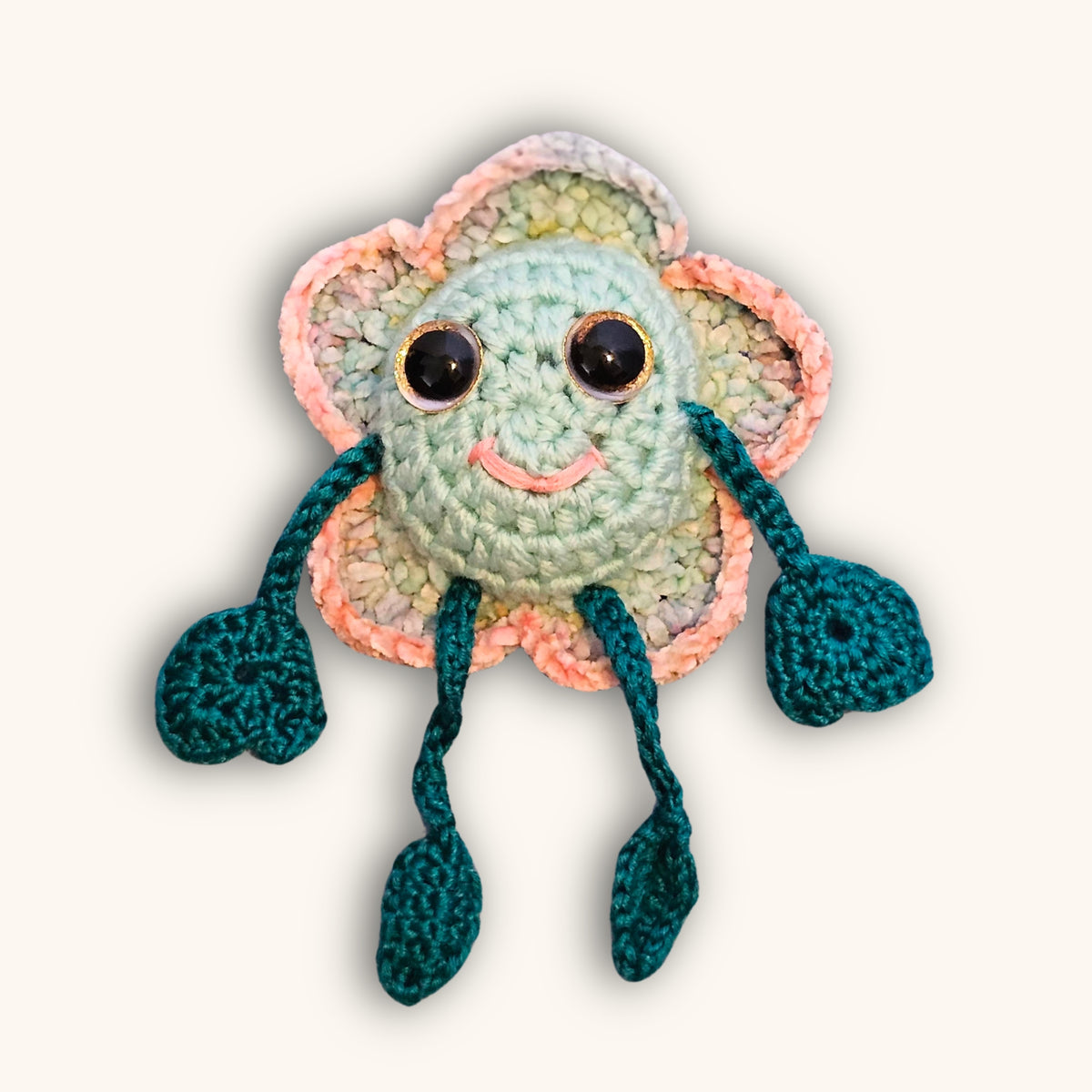 Floyd Flower Boy handmade crochet keepsake with a mint green face, pastel flower petals, teal limbs, pink smile, and sparkly eyes.