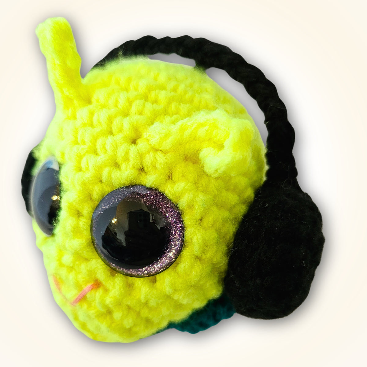 Angled view of Groovy Gus showing his neon face, purple-rimmed sparkly eyes, black side detail, and thick rounded crochet construction.