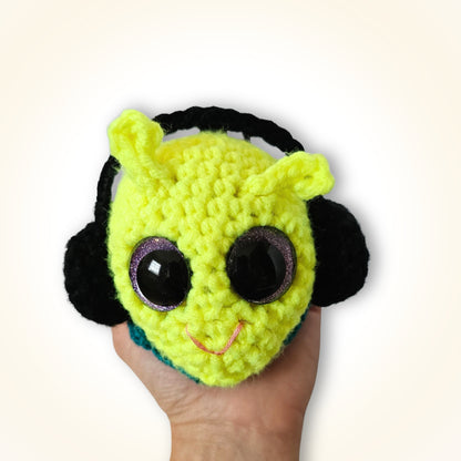 Groovy Gus resting in a hand, showing his neon yellow-green crochet face, large sparkly eyes, black side details, and rounded handmade construction.