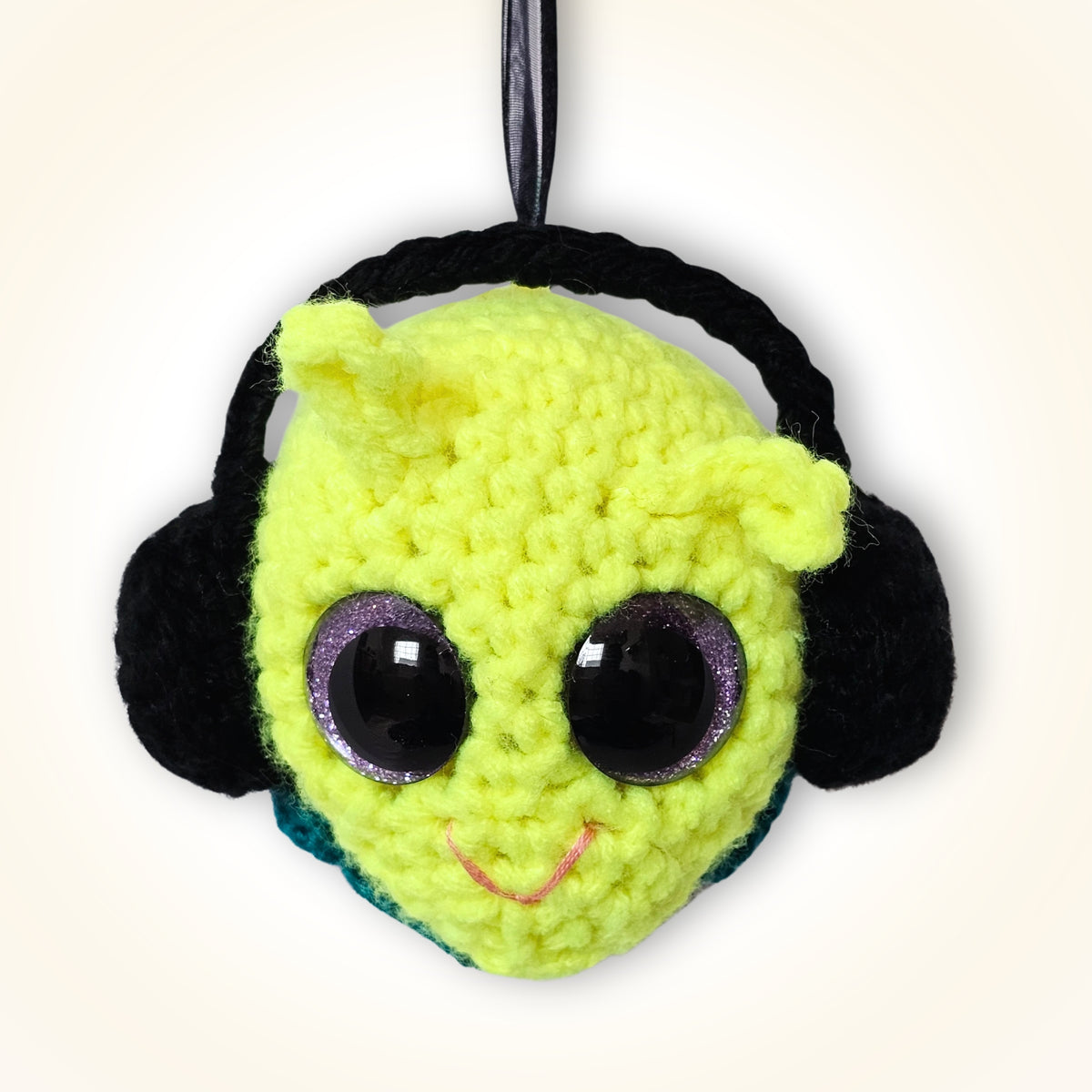Groovy Gus handmade crochet decorative keepsake with a neon yellow-green face, black side details, purple-rimmed sparkly eyes, pink smile, and black hanging ribbon.