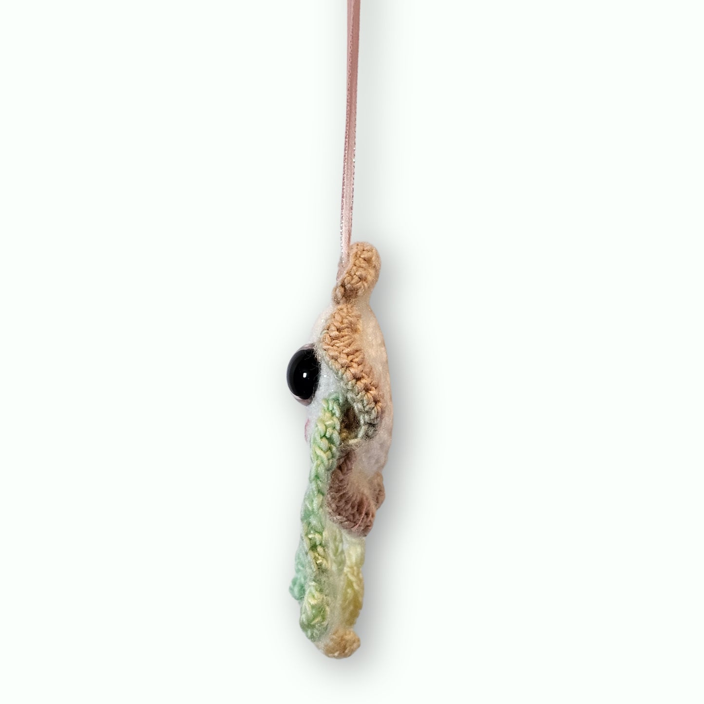 A handmade crochet fish ornament with a black bead eye, hanging from a thin pink ribbon against a plain white background.