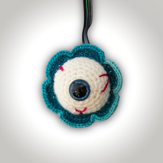 Iris Oddball handmade crochet eyeball keepsake with a large blue-rimmed eye, red stitched veins, and a teal scalloped outer edge.