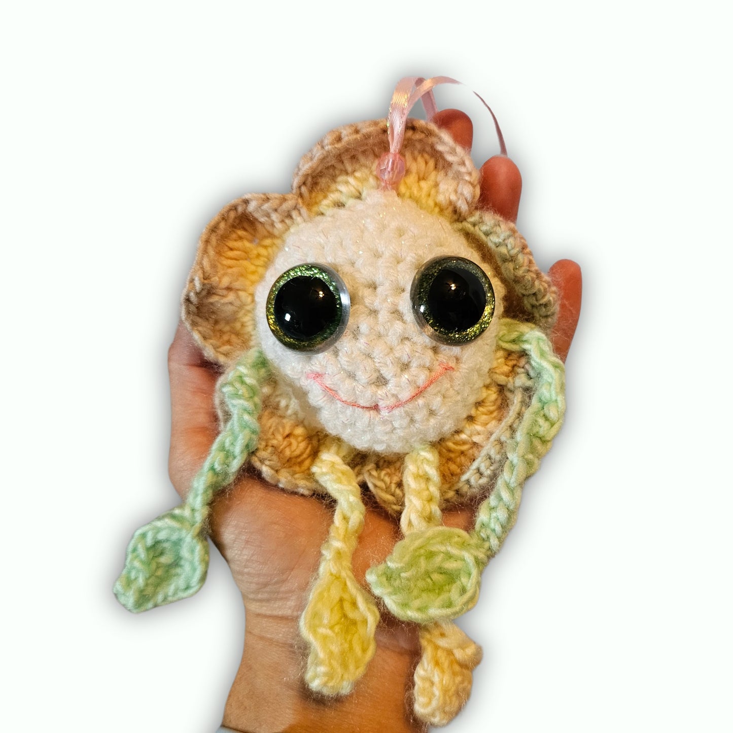 A handmade crocheted plush ornament shaped like a smiling sunflower, held in a person's hand against a plain white background.