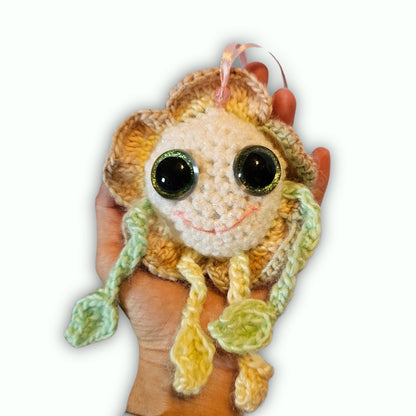 A handmade crocheted plush ornament shaped like a smiling sunflower, held in a person's hand against a plain white background.