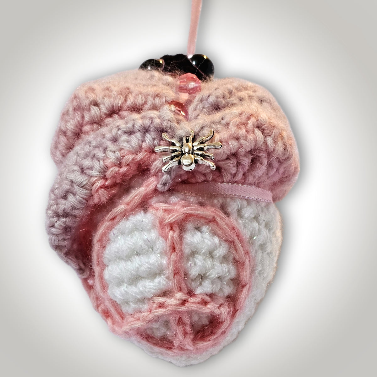 Back view of Skelly Rose showing layered pink and purple crochet petals, bead accents, a metallic spider, and a peace-sign-inspired design.