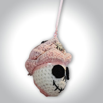 Angled side view of Skelly Rose showing the dimensional white crochet skull, layered pink-to-purple flower petals, and pink hanging ribbon.