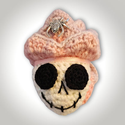 Skelly Rose handmade crochet skull keepsake with a white sparkly skull face, black eye sockets, pink flower petals, metallic spider, and pink hanging ribbon.