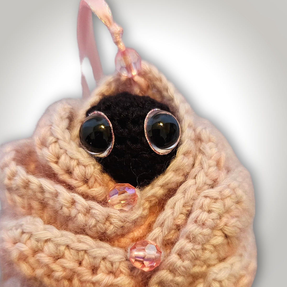 Close-up of the tiny black crochet sprite with sparkly pink eyes peeking from the layered flower petals on the back of Skelly Rose.