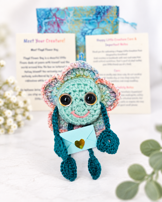 Handmade mint green crochet flower creature named Floyd Flower Boy holding a small light blue mystery message envelope.