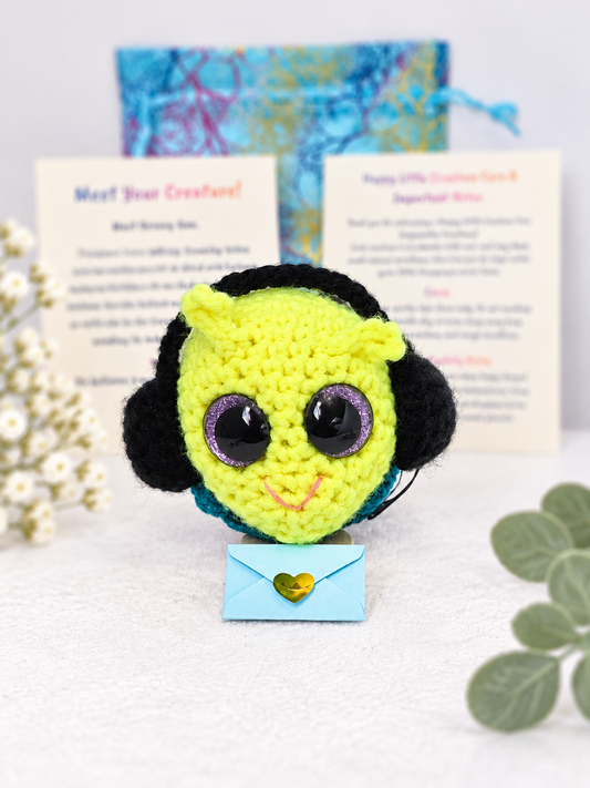 Handmade neon yellow-green crochet creature named Groovy Gus holding a small light blue mystery message envelope.