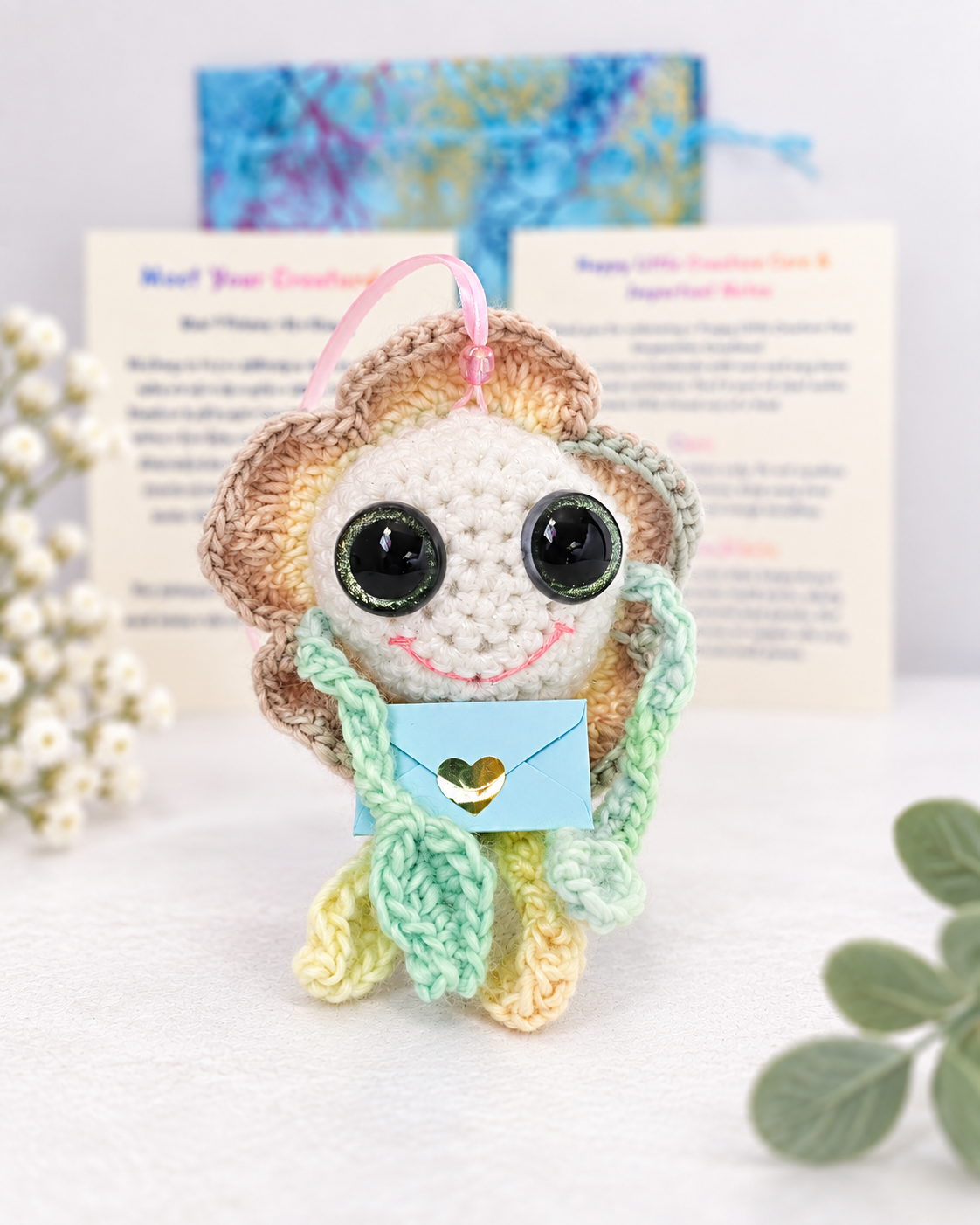 Handmade crochet marigold flower creature named Mellow Marigold holding a small light blue mystery message envelope.