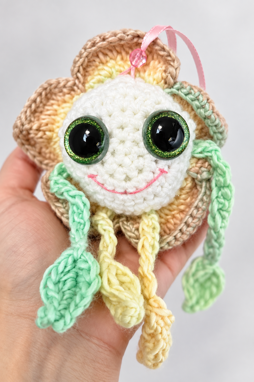 Side profile of Mellow Marigold held in a hand showing his green leafy limbs and layered yellow crochet petals.