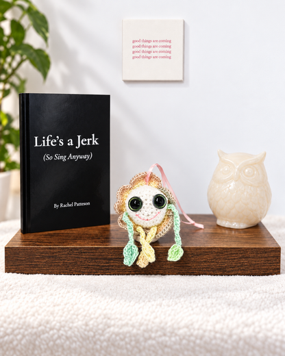 Mellow Marigold crochet keepsake sitting on a wooden display shelf next to the poetry book Life's a Jerk So Sing Anyway.  