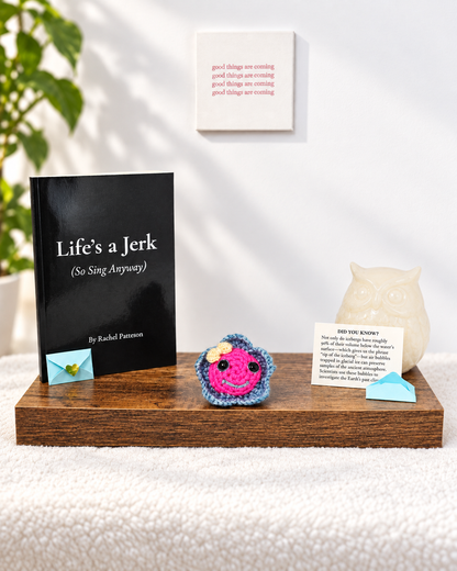 Pinky Bluefin crochet keepsake sitting on a wooden display shelf next to the poetry book Life's a Jerk So Sing Anyway.