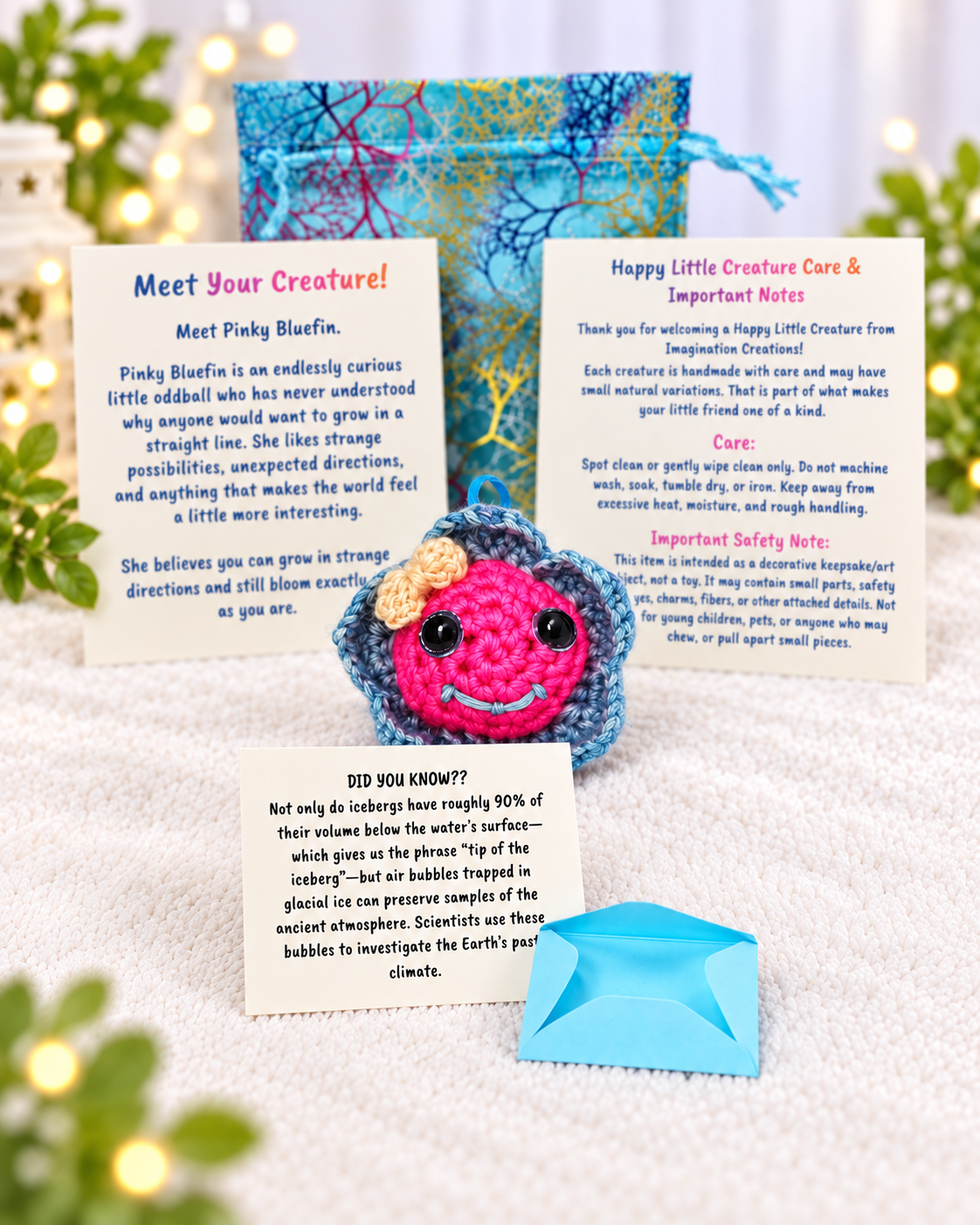 Complete unboxing set for Pinky Bluefin showing handmade crochet fish plush, printed personality card, mystery message envelope, and pouch.