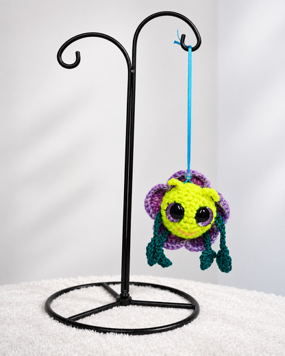 Pitalian the alien crochet ornament suspended from a black metal display stand.