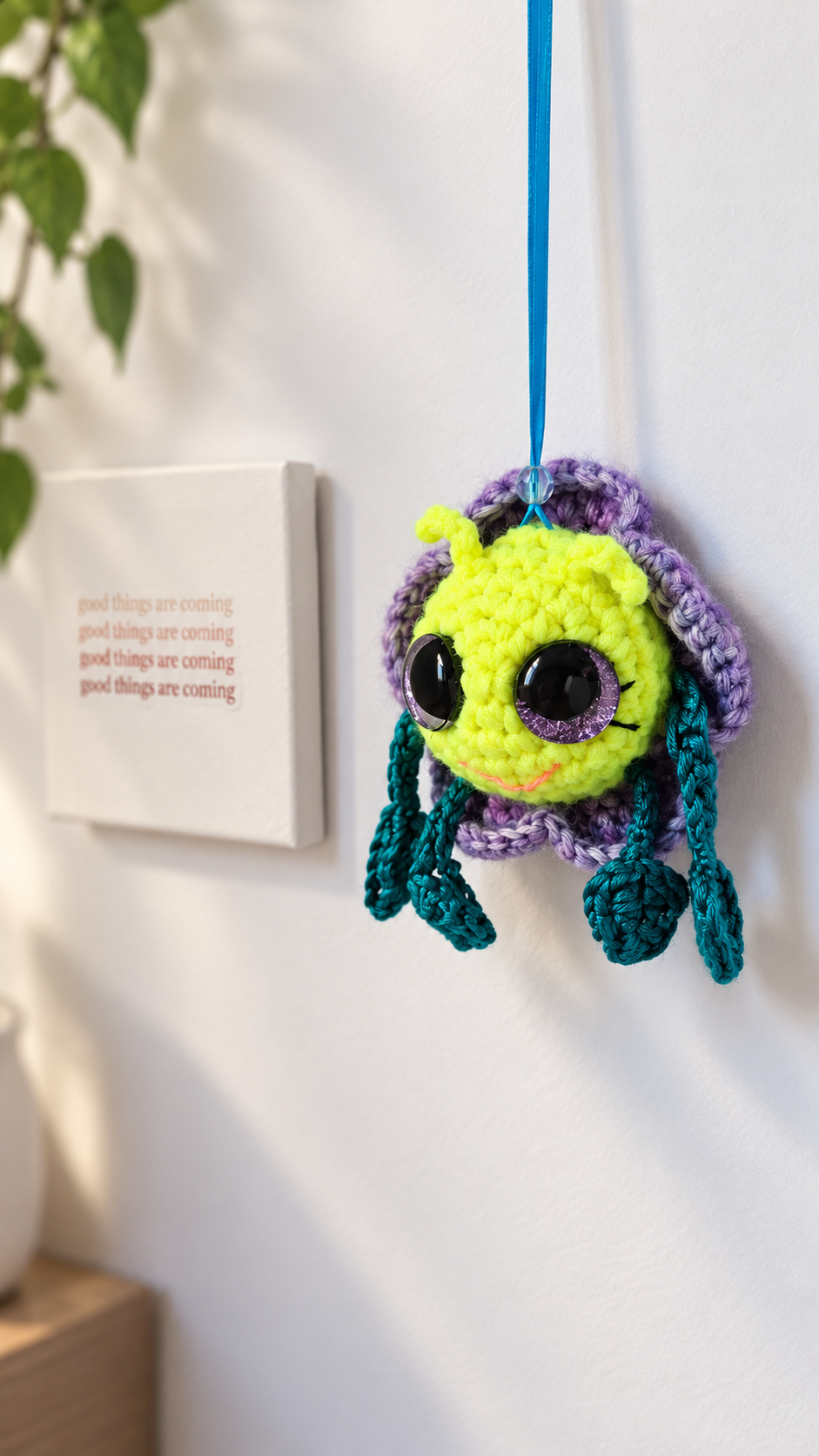 Pitalian the alien hanging by his blue ribbon against a neutral background.