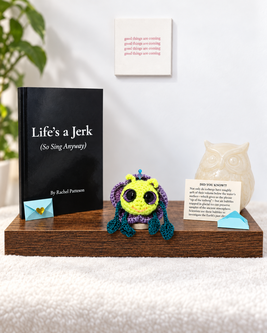Pitalian the alien crochet keepsake sitting on a wooden display next to the poetry book Life's a Jerk So Sing Anyway.  