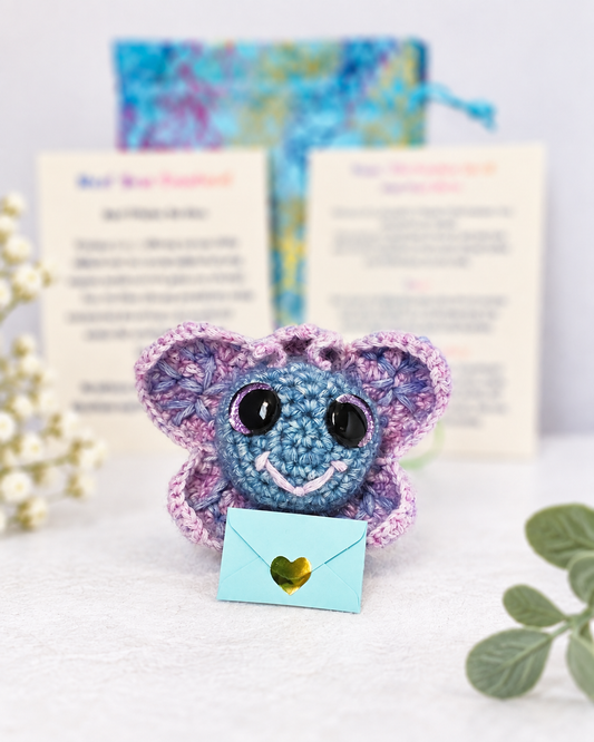 Handmade purple and blue crochet butterfly creature named Playful Pippa Purplewisp holding a small light blue mystery message envelope