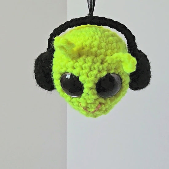 360-degree view of Groovy Gus, a handmade crochet decorative keepsake with a neon yellow-green face, black side details, purple-rimmed sparkly eyes, colorful layered back, and lavender peace sign.