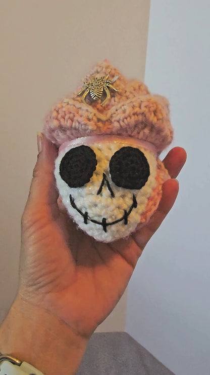 Close-up video of Skelly Rose, a handmade crochet skull keepsake with a sparkly white skull face, layered pink and purple flower petals, metallic spiders, beads, and a hidden black sprite with pink sparkly eyes.