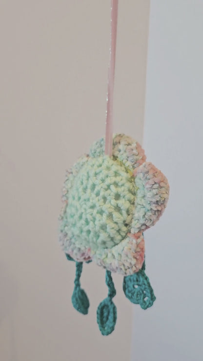 360-degree view of Floyd Flower Boy, a handmade crochet flower keepsake with a mint green face, pastel flower petals, teal dangling limbs, sparkly eyes, and a pink hanging ribbon.
